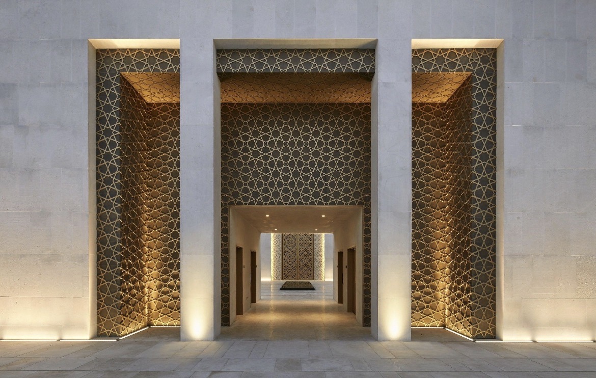 Three lit geometric-patterned portals in a modern stone mosque facade